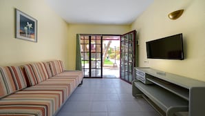 Un salon avec un canapé à rayures, un téléviseur fixé au mur et une porte vitrée donnant sur l’extérieur.