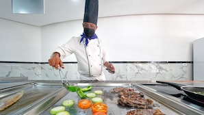Un chef cuisinant sur un gril, avec des légumes et de la viande.