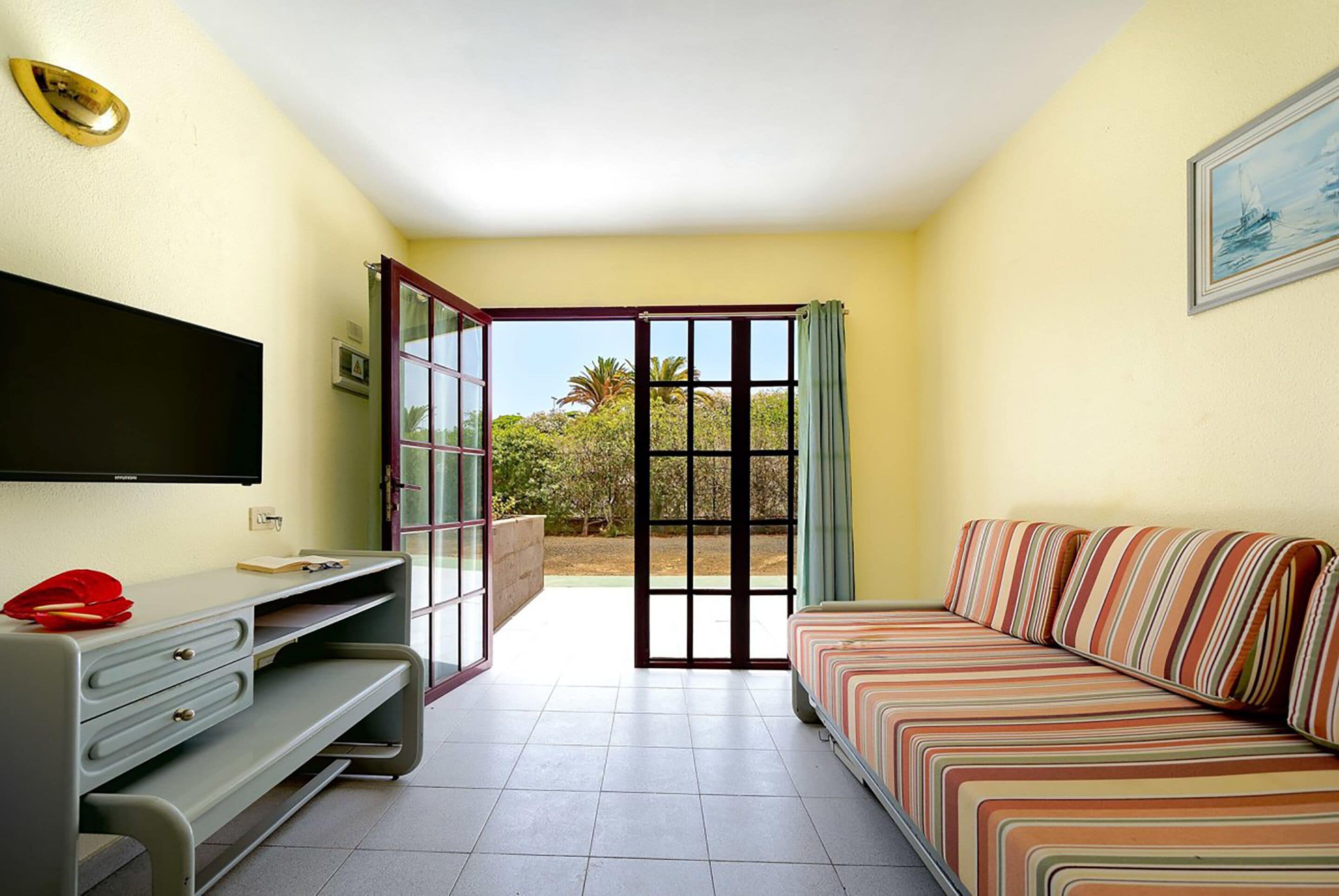 A room with a bed, a desk, a TV, and a sliding glass door leading to an outdoor area.