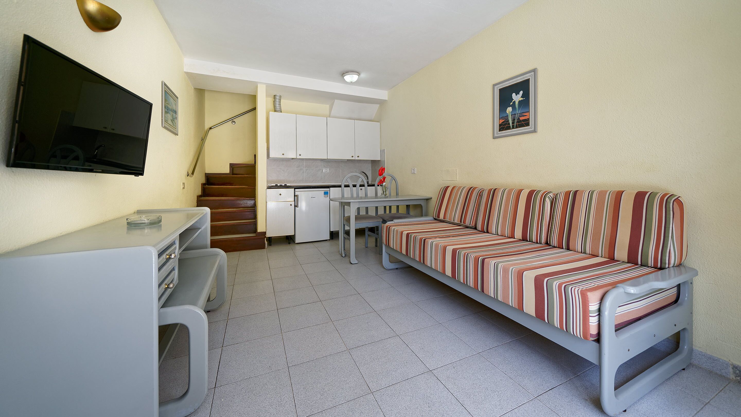 A compact living space with a kitchenette, a sofa, a TV, and a staircase leading to an upper level.