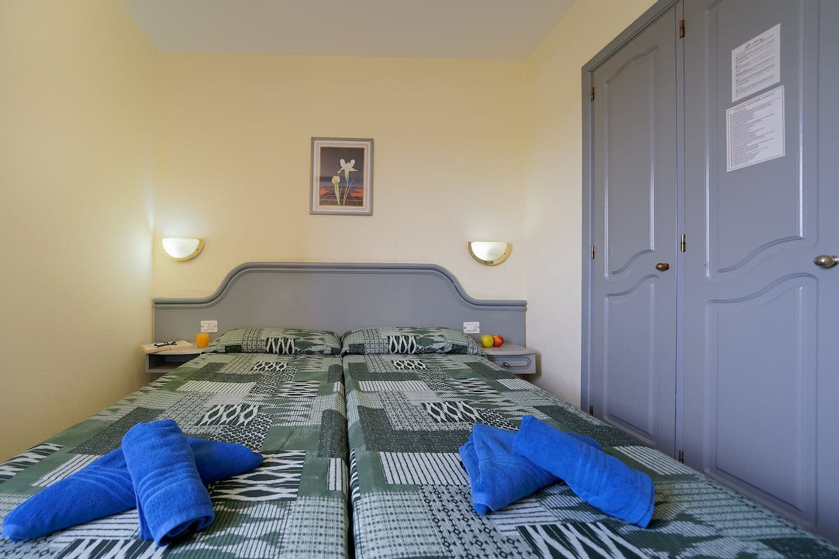 A single bed with patterned bedding, two bedside tables with lamps, a framed picture on the wall, and a wardrobe with a door.