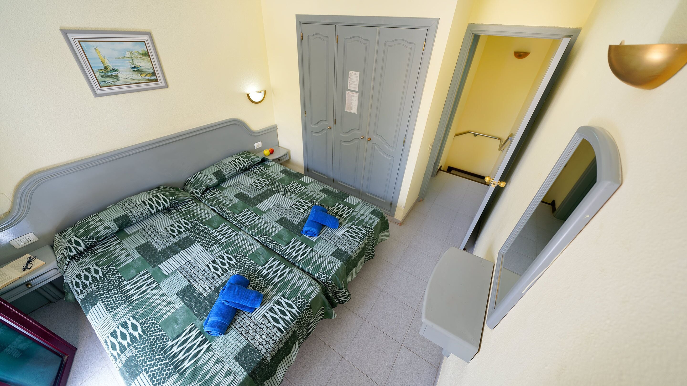 A room with a bed, a desk, a mirror, and a door.