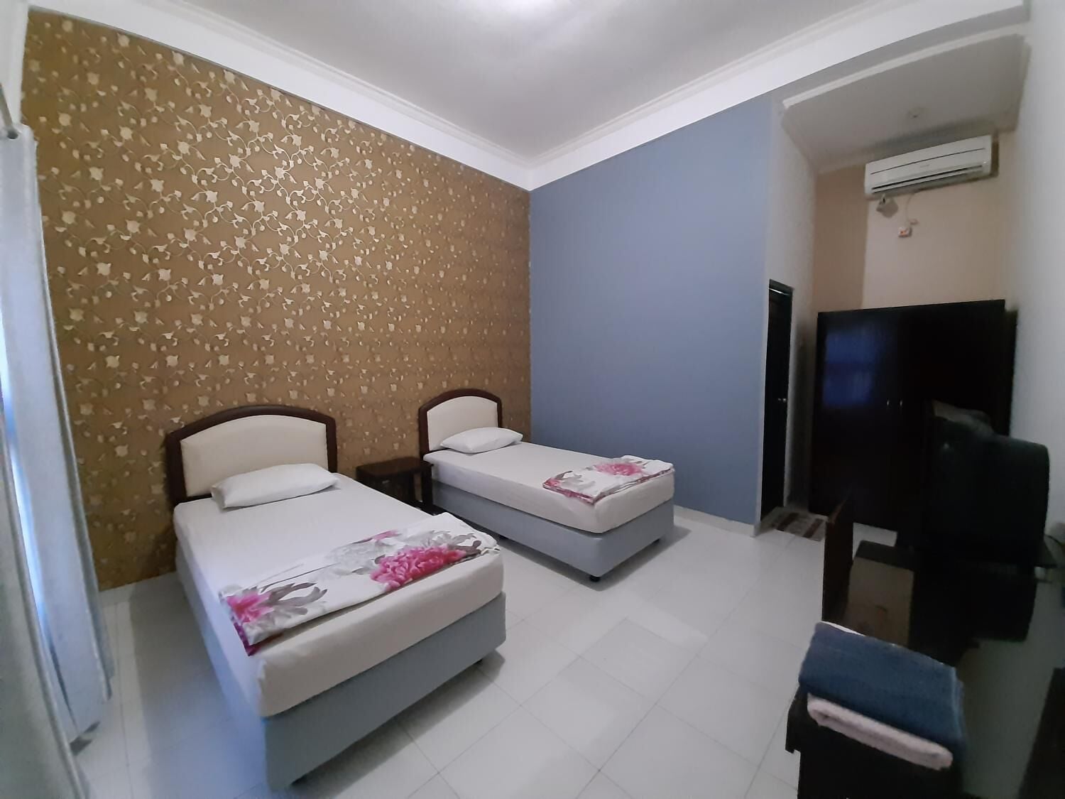 A hotel room with two beds, a TV, and an air conditioning unit.