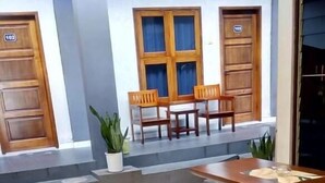 A seating area with wooden benches and tables, a potted plant, and a door with the number 102. - Wisma Liontine (Palangkaraya)