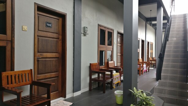 A hallway with wooden doors, a bench, a trash bin, and a staircase. - Wisma Liontine (Palangkaraya)