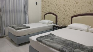 A hotel room with two single beds, a small bedside table with a lamp, and a curtain on the window. - Wisma Liontine (Palangkaraya)