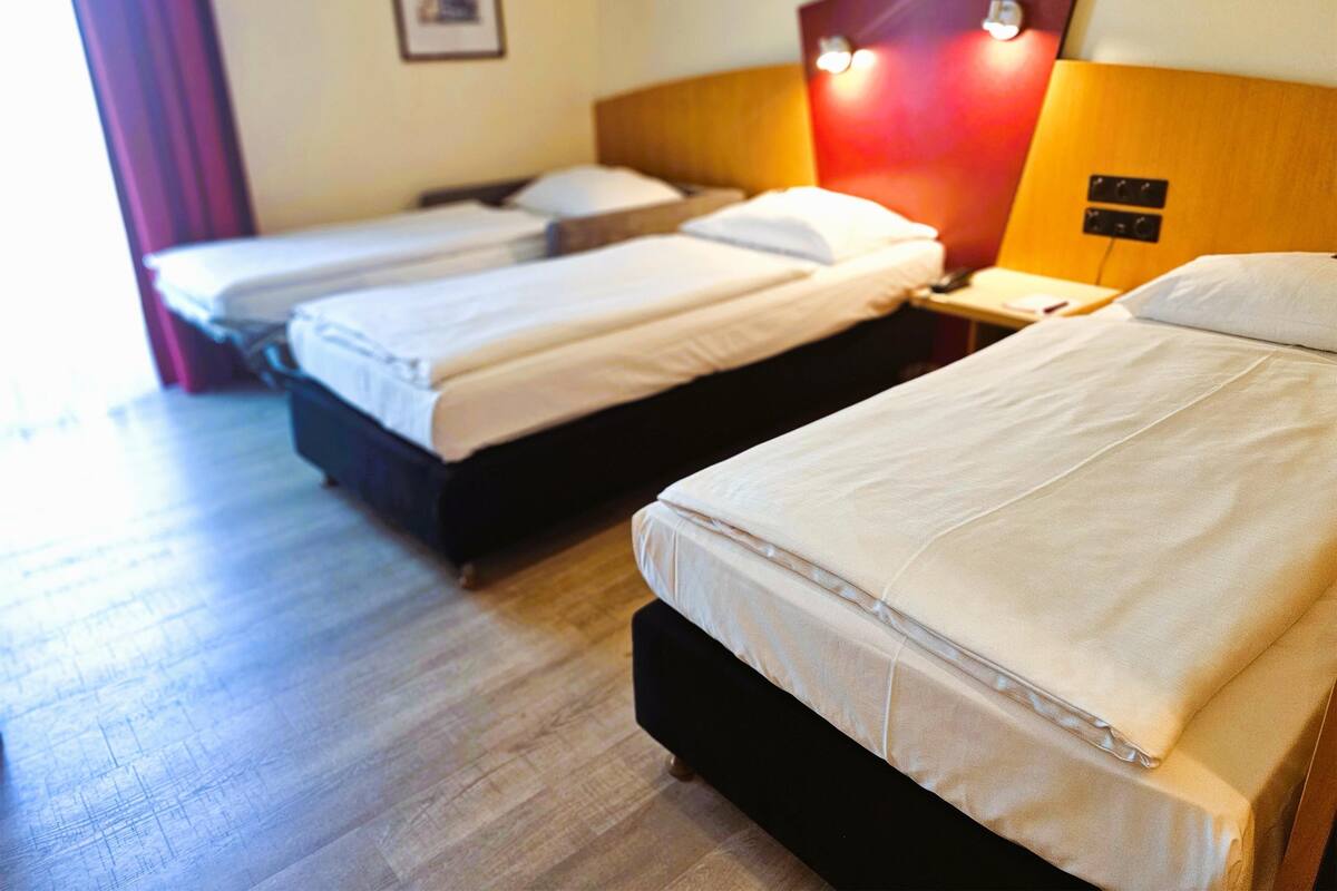 Habitación de hotel con tres camas individuales, cabeceros de madera y una pared de acento roja.