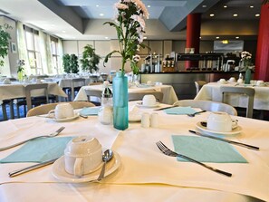 A dining area with tables set for tea service, complete with teacups, saucers, and a vase with flowers. - Arvena Park Das Hotel am Franken-Center (Nuremberg)