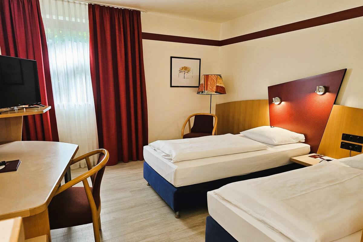Una habitación de hotel con dos camas, un escritorio, una silla, un televisor y una lámpara.