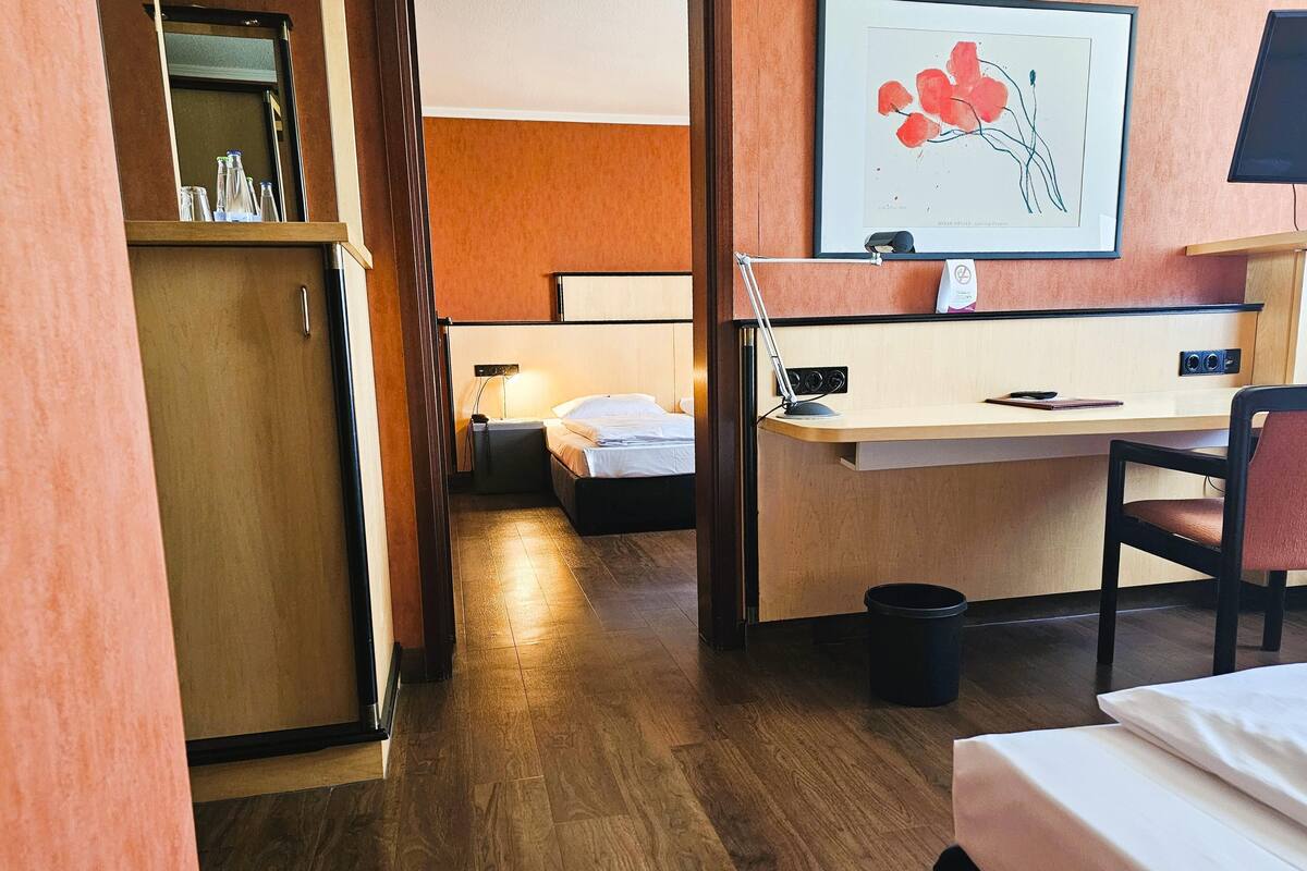 Una habitación de hotel con un escritorio de madera, una cama, una silla y un cesto de basura pequeño.
