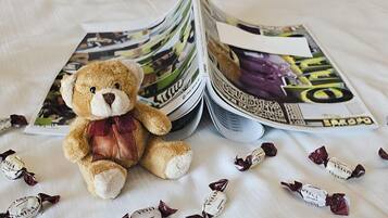 Un oso de peluche sobre la cama, junto a revistas y bombones.