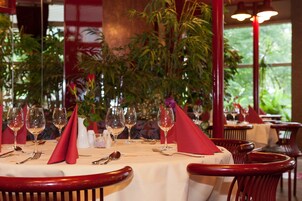 Mesa de restaurante dispuesta con copas de vino, cubiertos y servilletas rojas.
