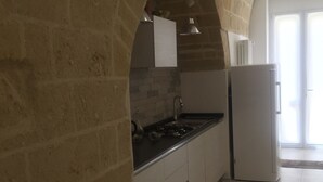 A kitchen with a stone archway, a white refrigerator, and a tiled floor. - Recinto Antico Sweet Rooms (Matera)