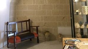 A room with a brick fireplace, a wooden bench, a glass display cabinet with pottery, and a small table with magazines. - Recinto Antico Sweet Rooms (Matera)
