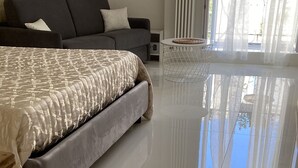 A modern bedroom with a large bed, a grey sofa, and a small side table. - Recinto Antico Sweet Rooms (Matera)