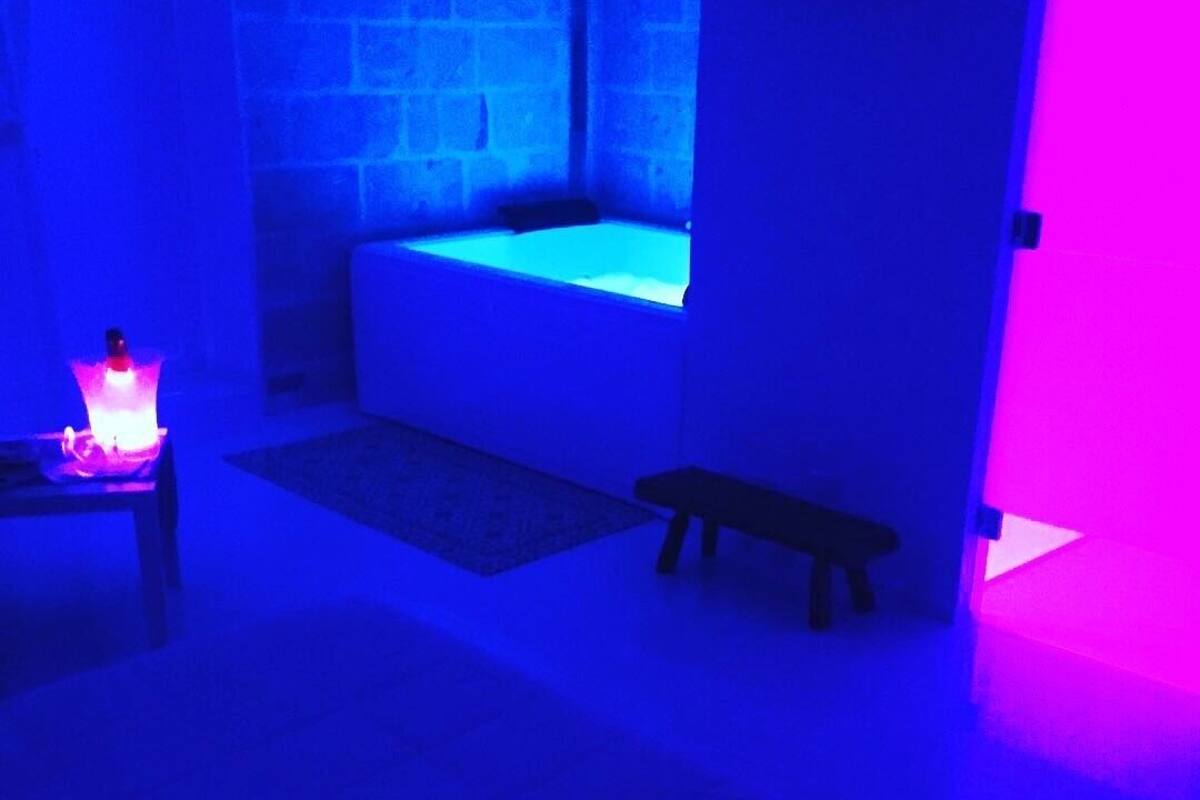 Una habitación con bañera, un banco y una mesita con luz.