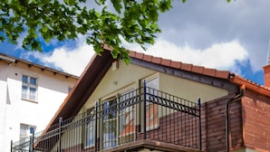 Un bâtiment à deux étages doté d’un balcon, d’une entrée fermée par un portail et d’un espace extérieur aménagé avec des chaises.