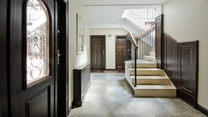 Un couloir avec une porte en bois sombre, un escalier doté d’une rampe et un radiateur fixé au mur.