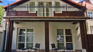 Une maison à deux étages dotée d’un balcon, de grandes fenêtres et d’une terrasse avec des meubles d’extérieur.