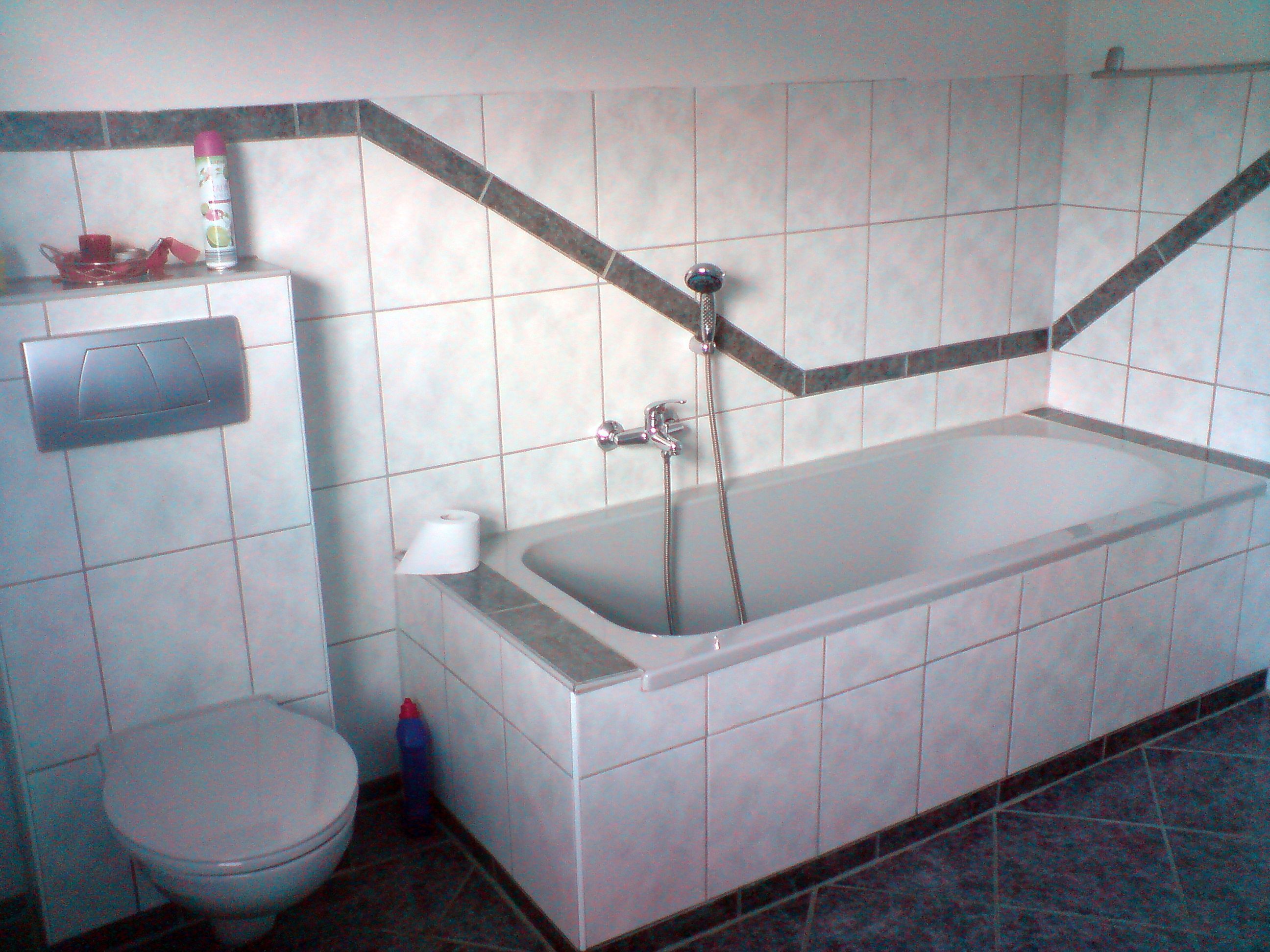 Et badeværelse med badekar, toilet og bruseniche.