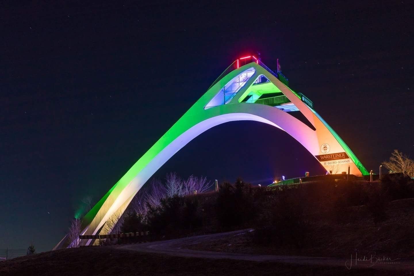 A brightly lit arch structure with a sign reading "Warsteiner St. Georg-Schanze" at its peak.