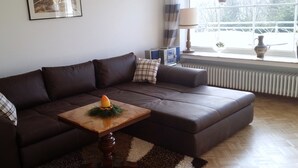 Un salón con un sofá de cuero marrón, una mesita de madera con una vela y un radiador cerca de una ventana.