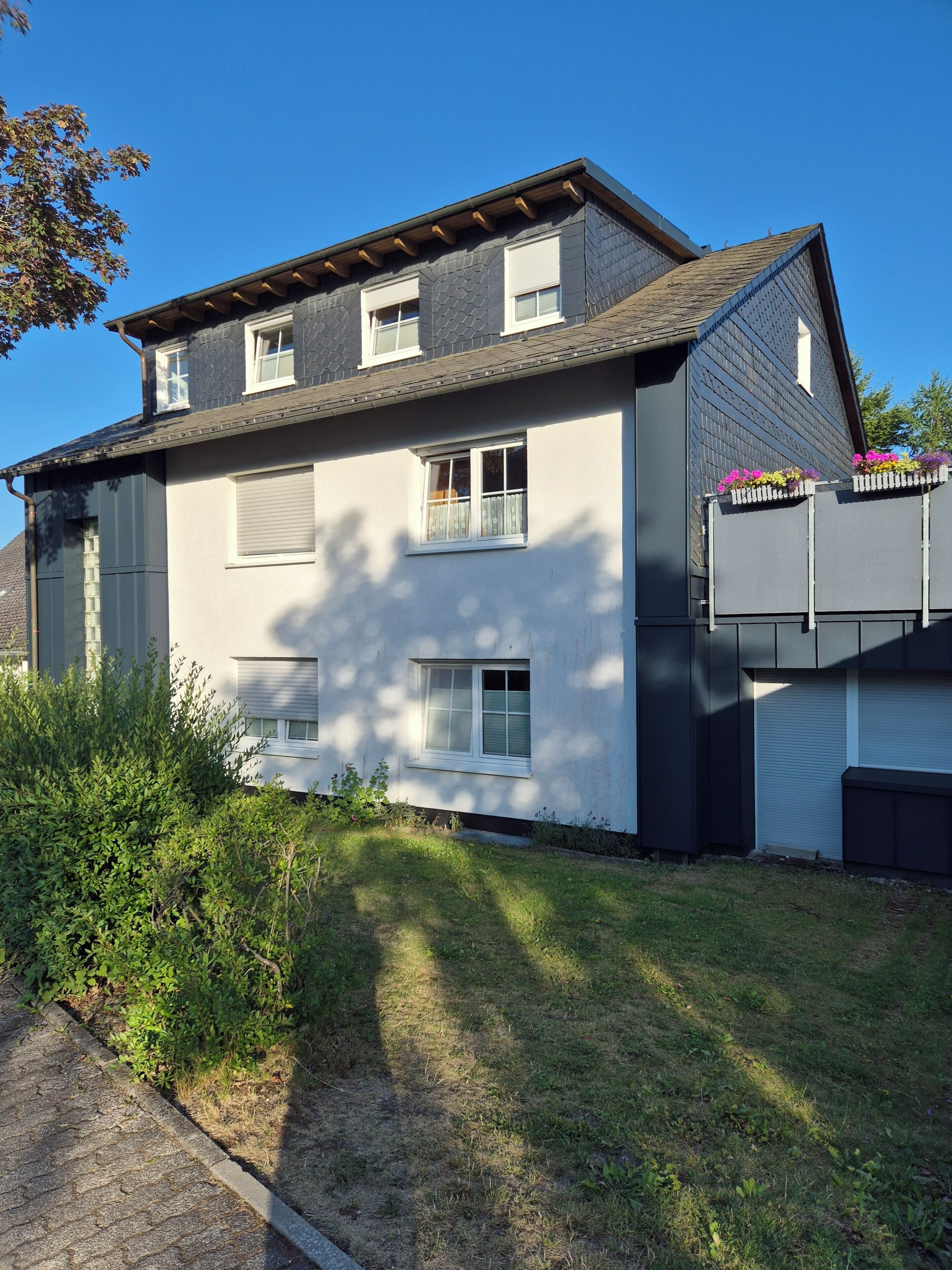 Une maison à deux étages, dotée d’un toit en pente, de nombreuses fenêtres et d’un petit jardin.