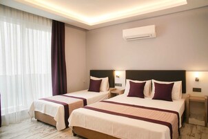 A hotel room with two beds, each with a headboard, bedside tables, and a wall-mounted air conditioner.