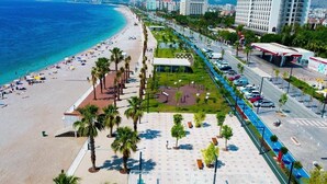 A coastal cityscape with a beach, palm trees, a parking area, and a gas station. - Af-Ra Hotel (Konyaalti)