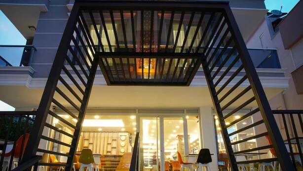 A modern building entrance with a glass facade, outdoor seating area, and a staircase leading to the entrance. - Af-Ra Hotel (Konyaalti)