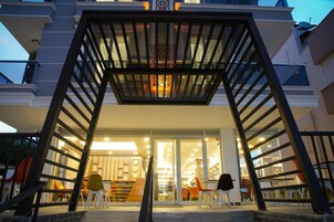 A modern building entrance with a glass facade, outdoor seating area, and a staircase leading to the entrance.
