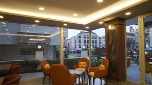 A modern indoor seating area with orange chairs and a small table, large windows, and a view of the cityscape. - Af-Ra Hotel (Konyaalti)