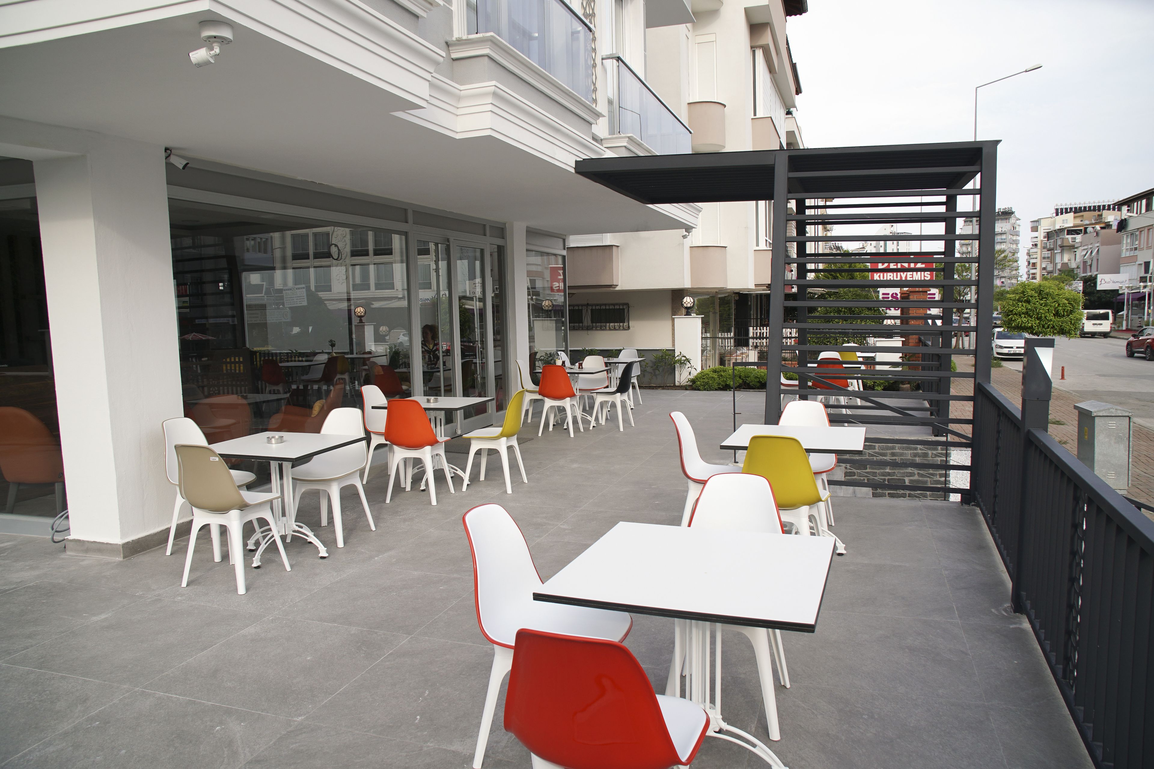 An outdoor cafe area with tables and chairs, a covered seating area, and a view of the street.