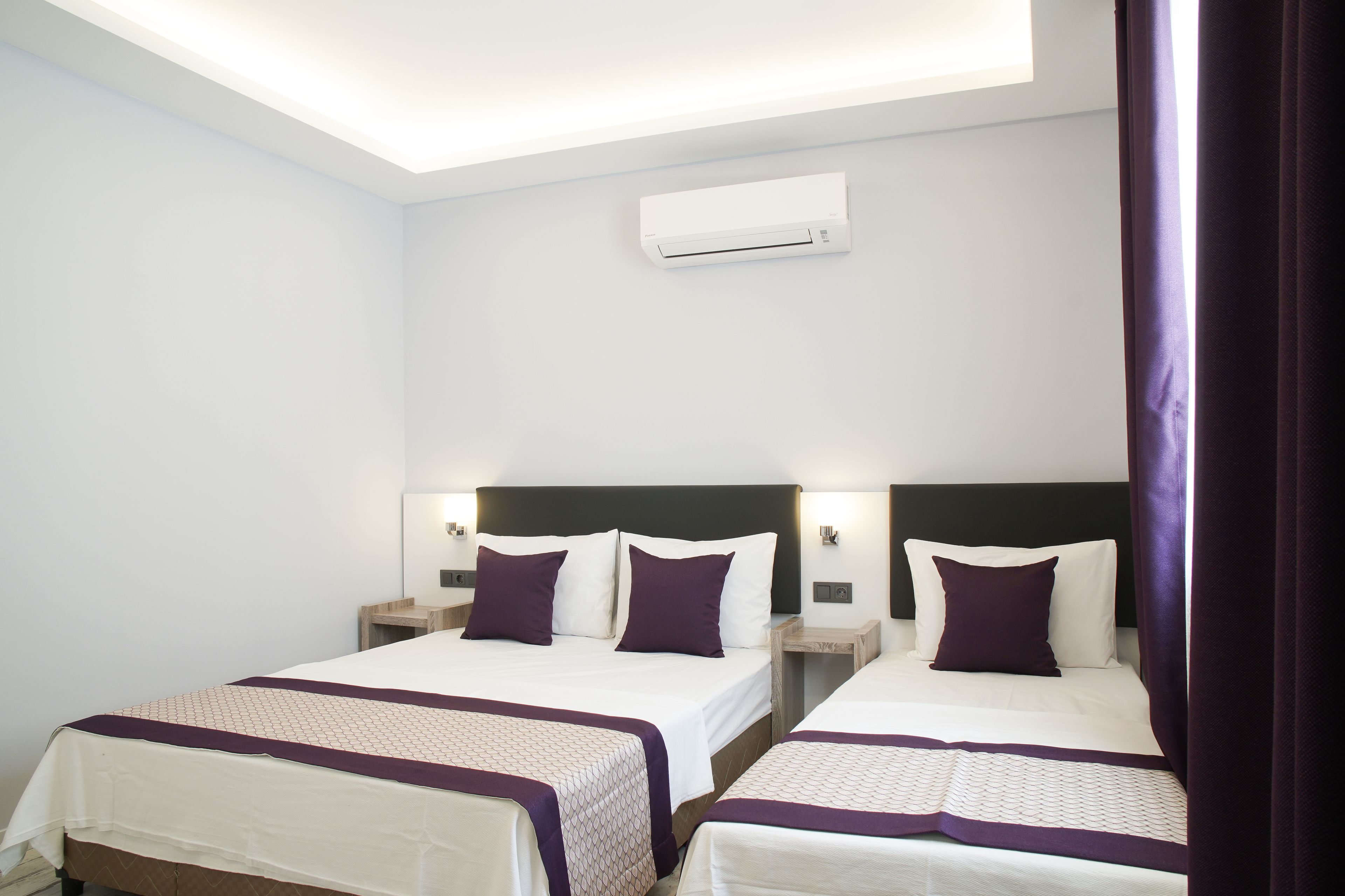 Habitación de hotel con dos camas, cada una con cabecera, mesitas de noche y aire acondicionado instalado en la pared.