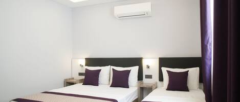Habitación de hotel con dos camas, cada una con cabecera, mesitas de noche y aire acondicionado instalado en la pared.