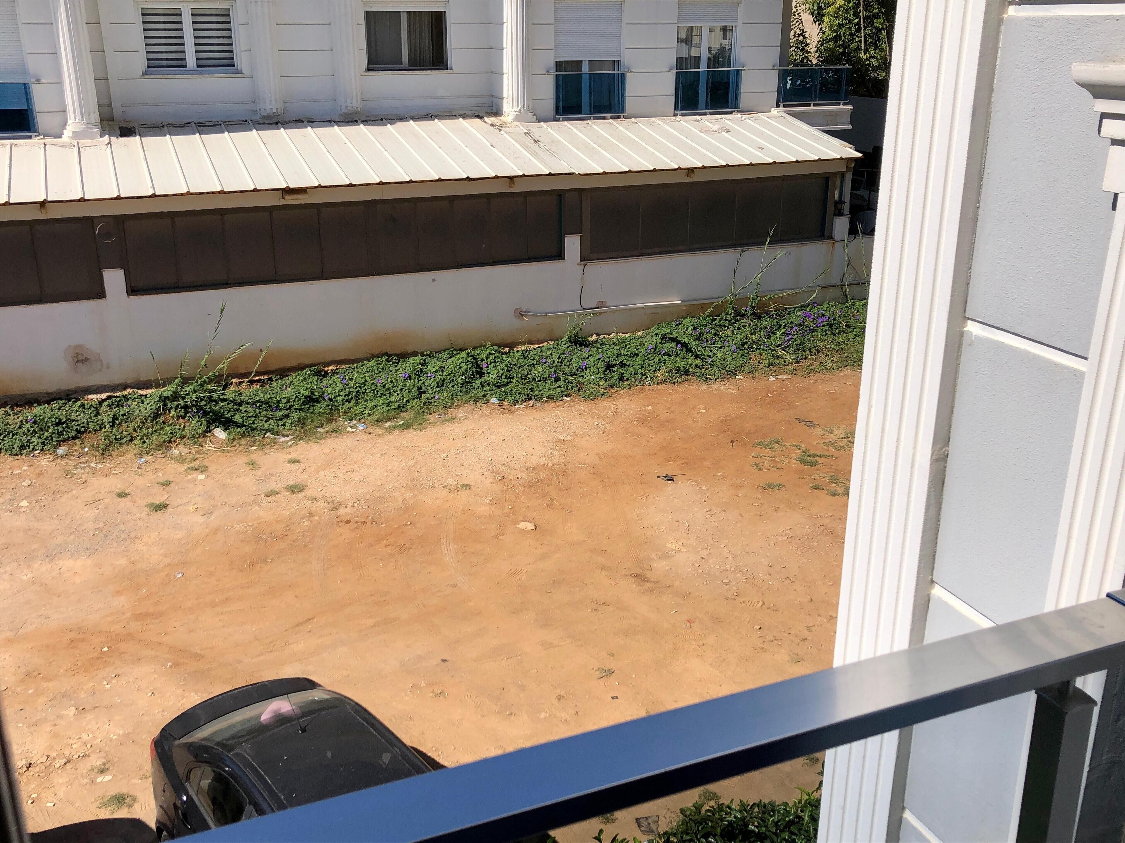 A view from a balcony overlooking a dirt ground with a building in the background.