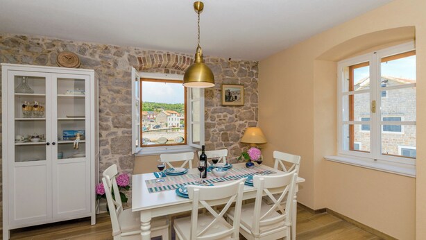 A dining area with a stone wall, a table set for four, and a view of a village through a window. - House Morko1 (Vrboska)