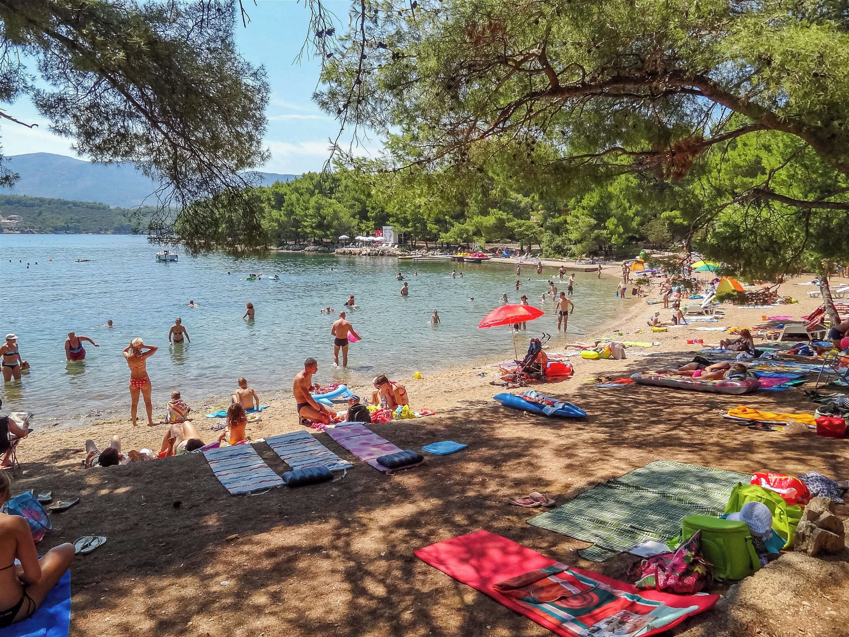 A beach with people swimming and sunbathing, umbrellas, and beach chairs.