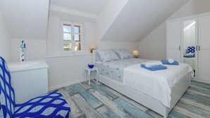 A bedroom with a sloped ceiling, a bed with striped bedding, a nightstand, a small table, a chair, and a wardrobe. - House Morko1 (Vrboska)