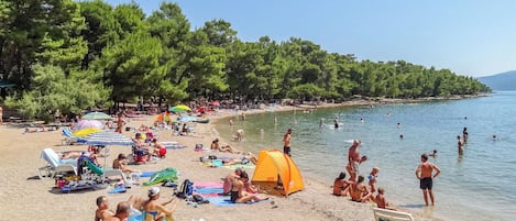 A beach with people sunbathing, swimming, and a tent set up.