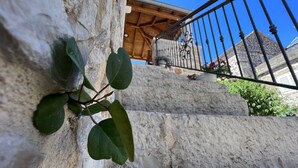 A stone wall with a plant growing on it, a wooden staircase, and a metal railing. - House Morko1 (Vrboska)