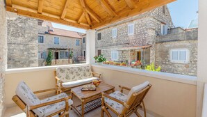 A covered outdoor seating area with a wooden table and chairs, overlooking a courtyard with stone buildings and a view of the surrounding area. - House Morko1 (Vrboska)
