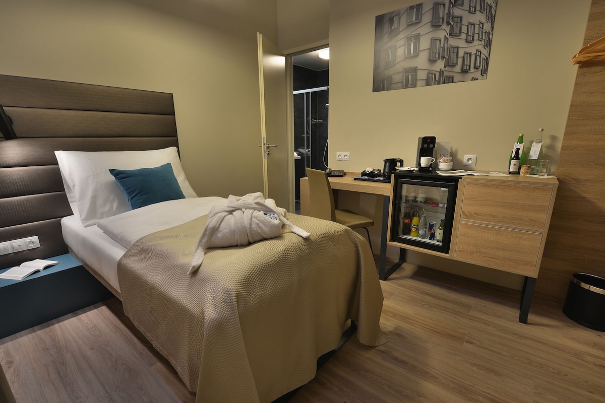 A hotel room with a bed, a desk, a minibar, and a shower area.