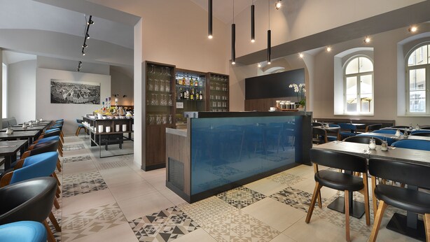 A modern restaurant with a central bar, blue and black chairs, and patterned floor tiles. - EA Hotel New Town (Prague)