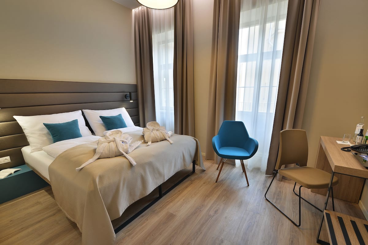 A hotel room with a bed, two chairs, a desk, and a window with curtains.