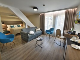 Quarto de hotel moderno com sofá, cadeiras, mesa de jantar e cama.
