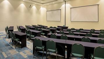 A conference room with rows of tables and chairs, a projector, and a screen.