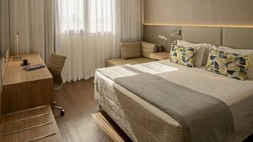 A hotel room with a bed, a desk, a chair, a nightstand, and a window with curtains.