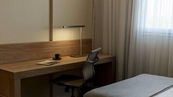 Habitación de hotel con un escritorio de madera, una silla, dos camas y una ventana con cortinas.