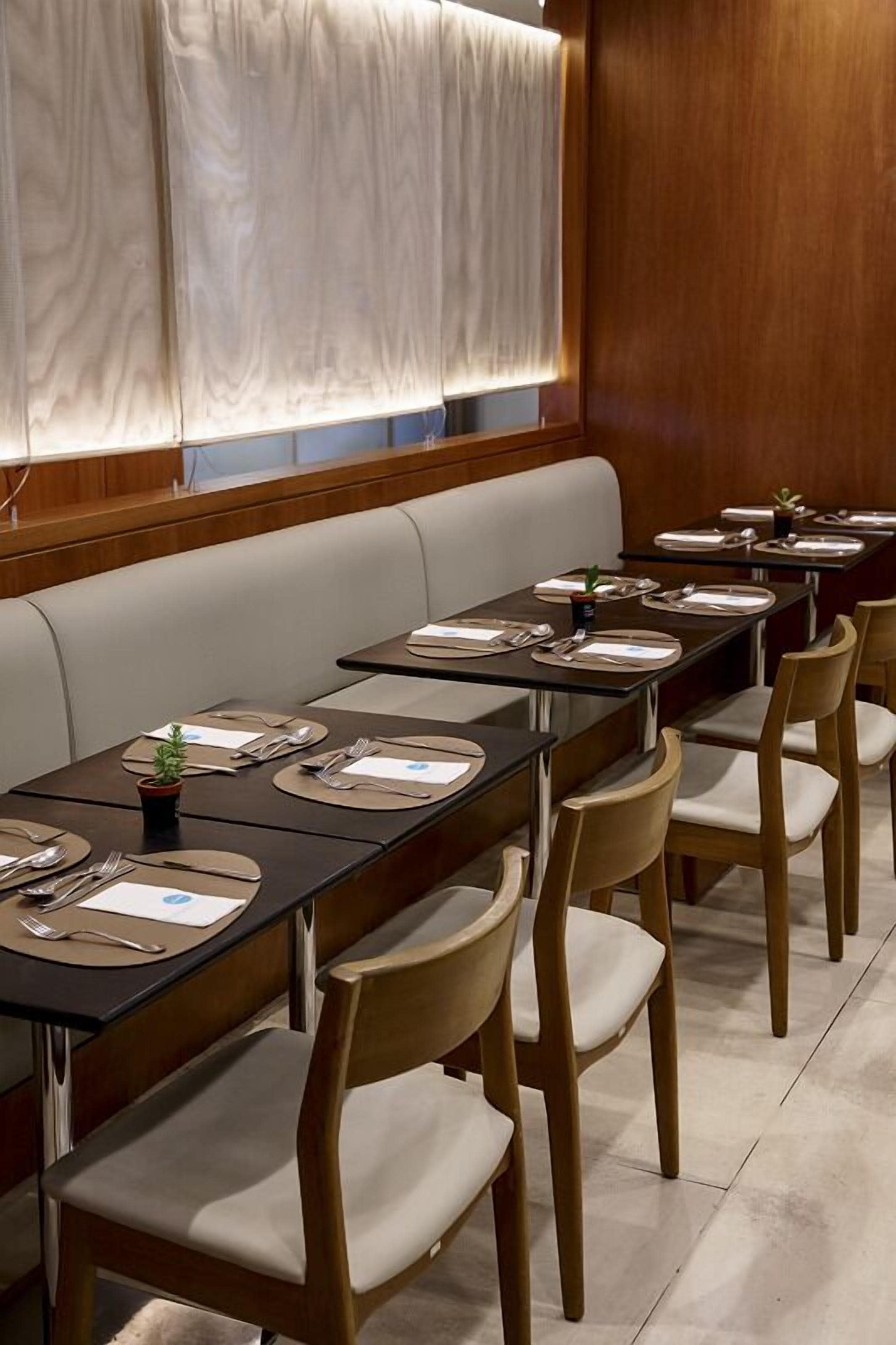 A restaurant with long tables, wooden chairs, and a cushioned bench.